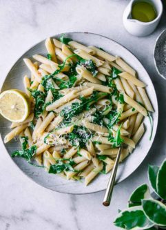 Penne，Arugula和Lemon Pasta在白板上，带有金叉在大理石台面上，带有绿色植物