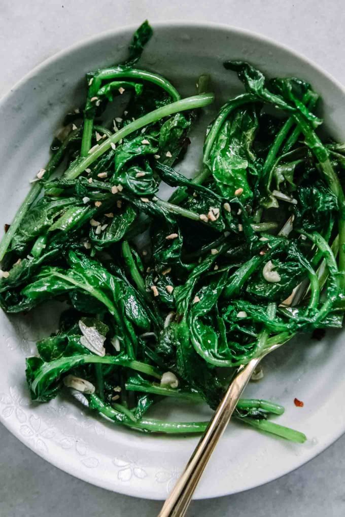 用金叉在白色盘子里用油和大蒜炒萝卜青菜